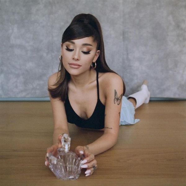 Ariana Grande boobs showing nice cleavage with her tits in a sexy black top bent forward promoting a perfume.